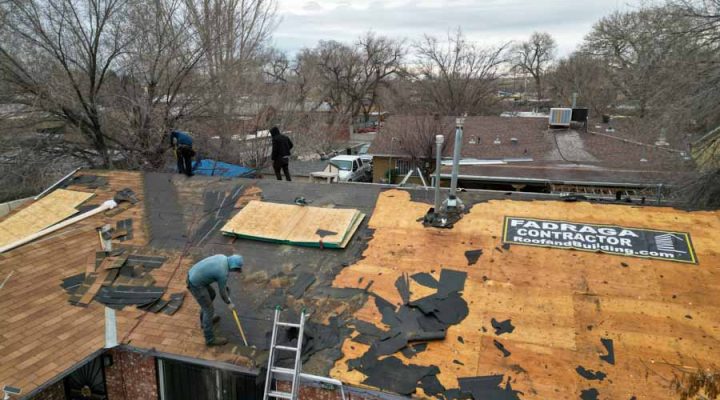 Team of contractors working on the roof of a house, removing old shingles and installing new underlayment.