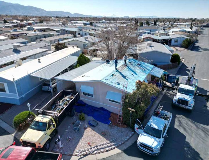 Residential Roof Replacement in a Neighborhood A neighborhood view showcasing a residential roof replacement project by Fadraga General Contractor, with workers installing a new roof underlayment and trucks parked around the property.
