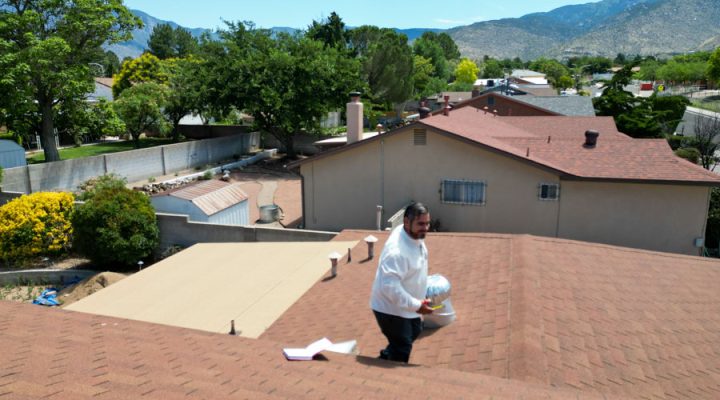 A professional assessing the condition of a roof with a notepad, located in a residential neighborhood with a mountain view.