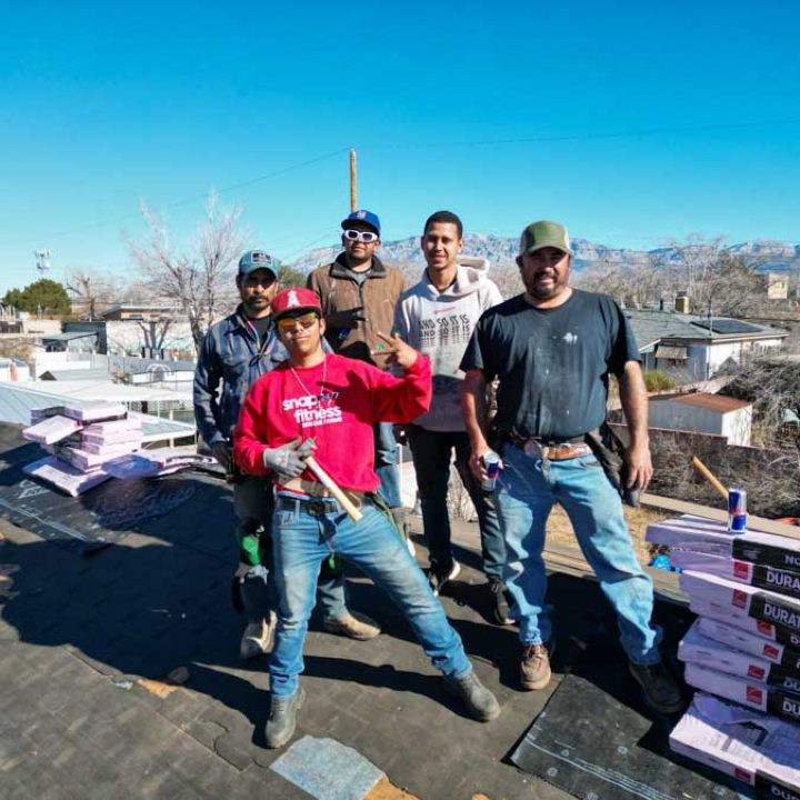 A cheerful roofing team posing on a house rooftop, showing unity and readiness to tackle roofing projects.